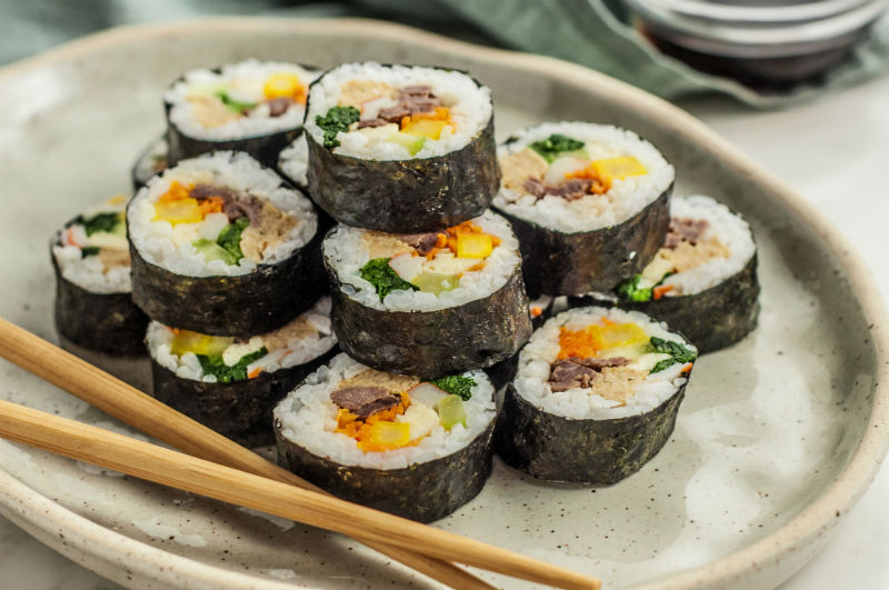 Gimbap is basically South Korean sushi, with the main difference being that the rice in the Japanese version is mixed with rice vinegar, sugar and salt while Gimbar is seasoned with salt and sesame oil. The rice and ingredients such as shrimp, spicy tuna, kimchi and squid are rolled in gim, which are dried sheets of nori seaweed, and served in bite-sized slices.